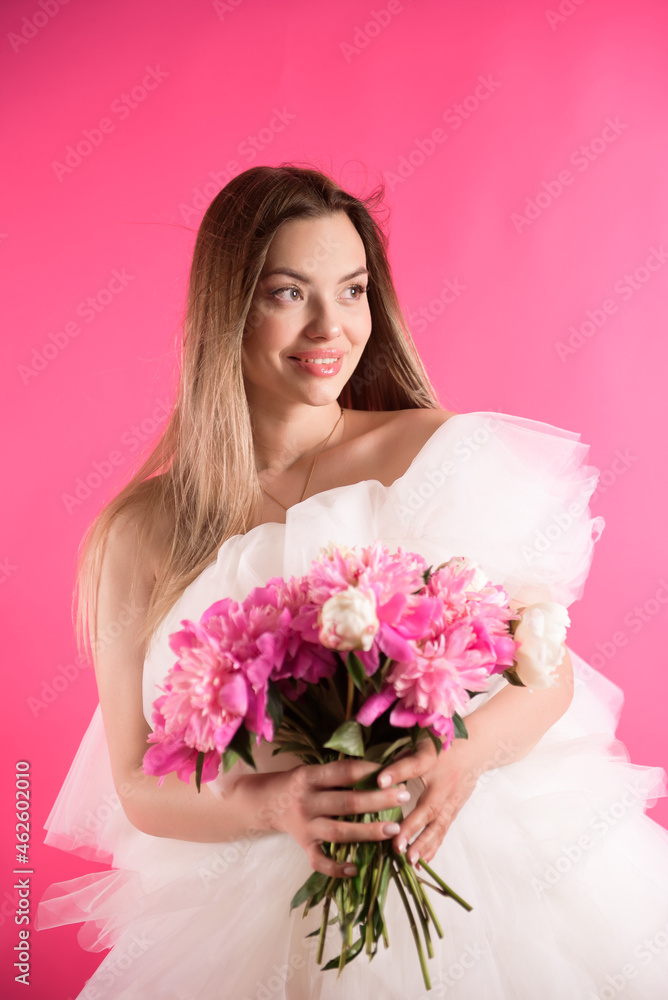 Portrait of a happy girl, holds in hands and smell and enjoying a bouquet of pink peony flowers.