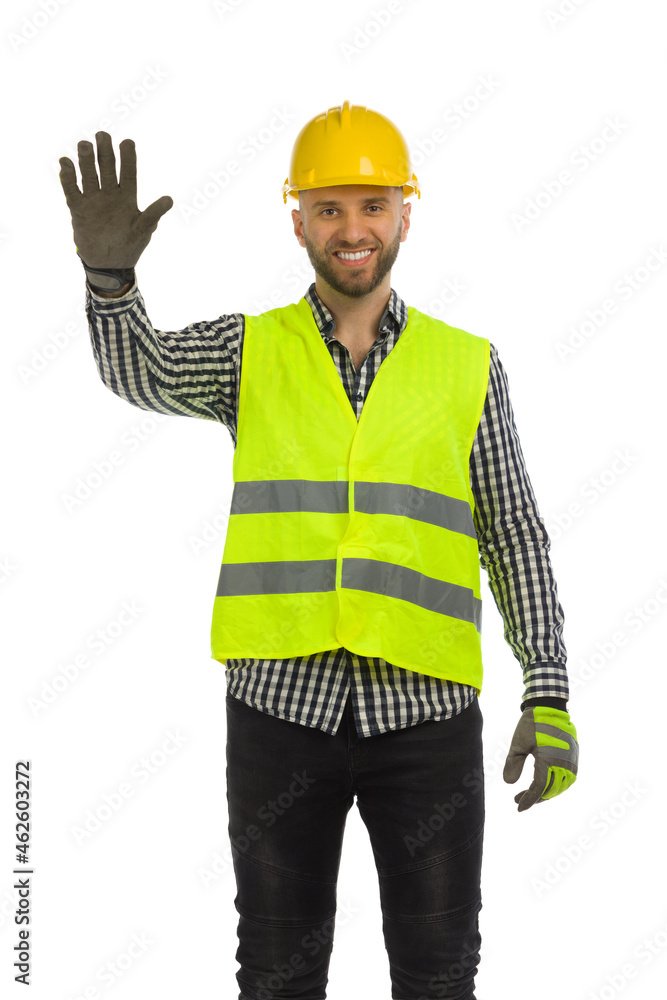 Smiling construction worker in reflective clothes is standing with hand raised. Stop gesture. Smiling construction worker in reflective clothes is standing with hand raised. Stop gesture.