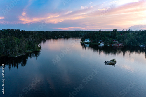 Beautiful purple pink sky reflects on calm still water with cottages on the shoreline.