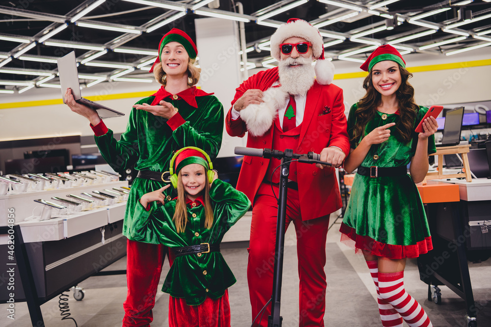 Photo of funny pretty santa claus assistants wear costumes smiling recommending you modern electronics indoors shopping center