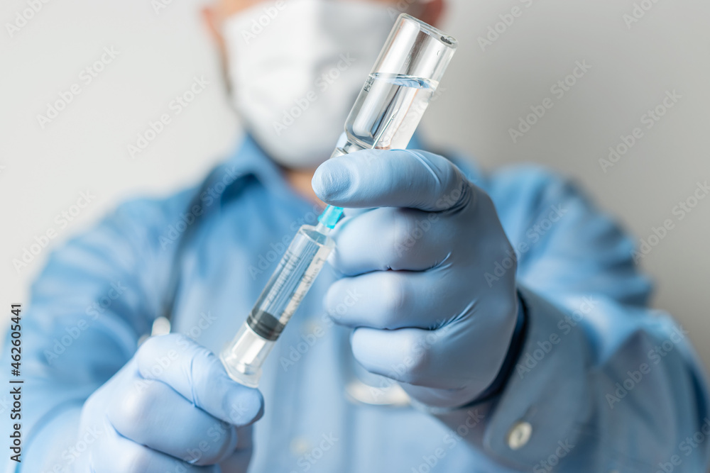 Male, doctor in blue shirt and gloves, holding in the hand a syringe and vaccine bottle against disease coronavirus or flu, vaccination concept Male, doctor in blue shirt and gloves, holding in the hand a syringe and vaccine bottle against disease coronavirus or flu, vaccination concept