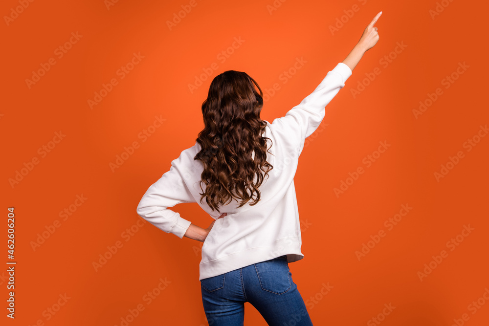 Back rear view photo of young girl indicate finger empty space wavy hair advertisement isolated over orange color background Back rear view photo of young girl indicate finger empty space wavy hair advertisement isolated over orange color background