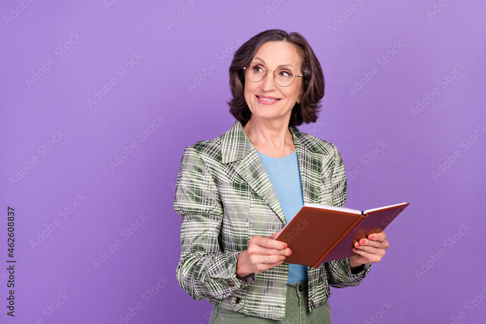 Photo of old dreamy happy lady hold hands book look empty space good mood isolated on violet color background Photo of old dreamy happy lady hold hands book look empty space good mood isolated on violet color background