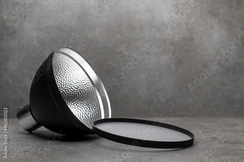 Diffuser cap and small speedlite flash light modifier reflector for illumination against a modern contemporary gray background. Photography accessory studio still life.
