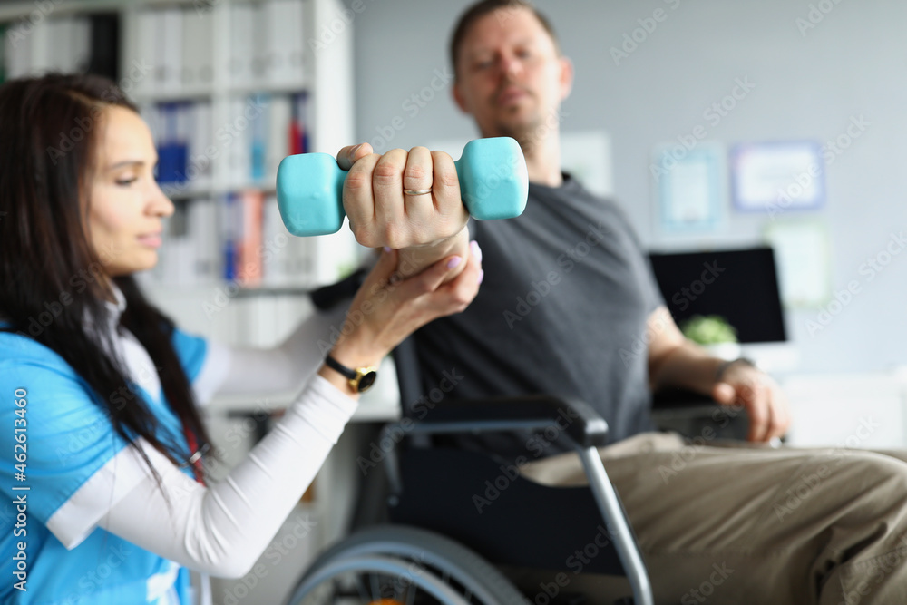 Fototapeta premium Rehabilitation therapist helping disabled man in wheelchair to lifting dumbbell in closeup