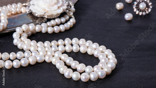 White luxurious pearl necklace on a black leather background. Shiny iridescent pearl jewelry close up. 