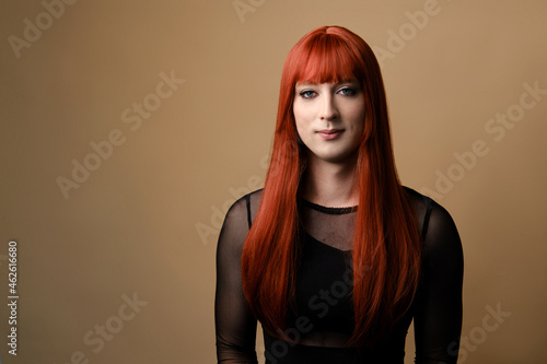 Transsexual woman. Portrait of young transgender woman in a red wig and makeup on a brown background. Concept diversity, transsexual, and freedom. photo