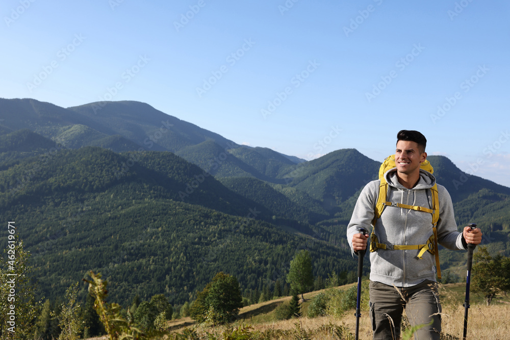 Tourist with backpack and trekking poles hiking through mountains, space for text