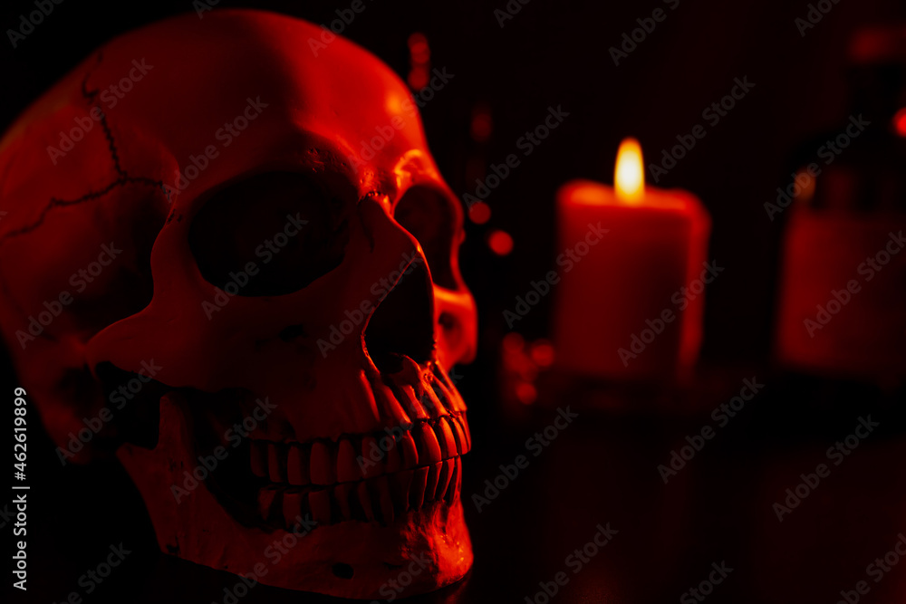 Close up of human skull in the spooky red light from the candle in background, Halloween concept Close up of human skull in the spooky red light from the candle in background, Halloween concept