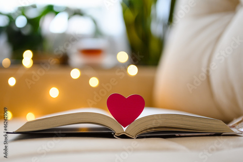 фотографія A small heart on an open book against the backdrop of a cozy home sofa and garland lights