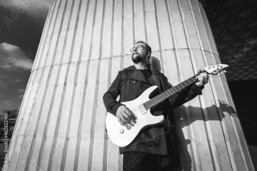Portrait of a man in black with a beard playing electric guitar on urban outdoor location