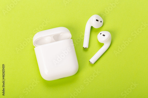 white wireless earbuds with charging case on green background