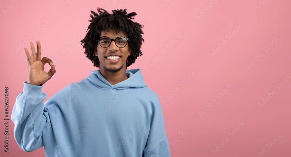 Portrait of happy African American teen guy showing OK gesture over pink studio background, panorama with blank space Portrait of happy African American teen guy showing OK gesture over pink studio background, panorama with blank space