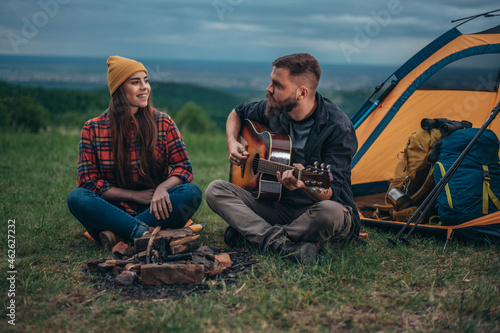 Couple of campers spending time together in the nature while playing guitar