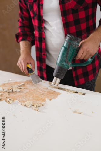 man removing old paint from he door using heat gun photo