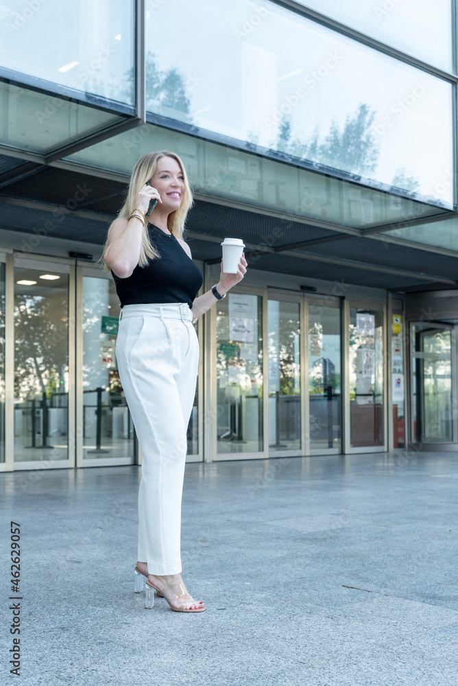 blonde woman talking on mobile phone in front of an office building blonde woman talking on mobile phone in front of an office building