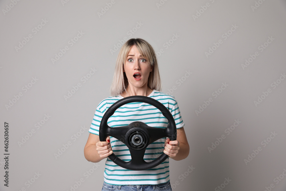 Fototapeta premium Emotional woman with steering wheel on grey background