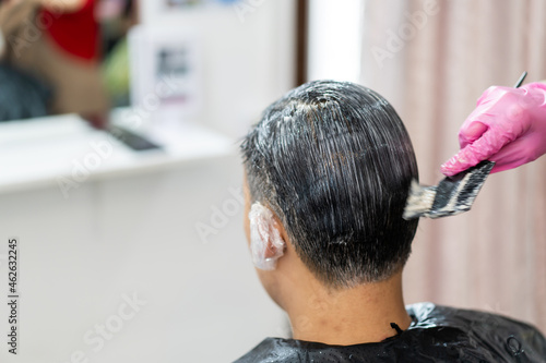 Asian young man making a hair dye at hair salon and spa. Professional hair stylist coloring - dying hair in male salon.