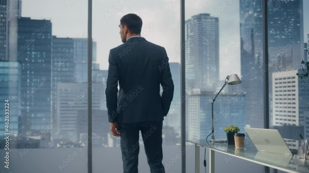 Thoughtful Young Businessman in a Perfect Tailored Suit Standing in His Modern Office Looking out of the Window on Big City with Skyscrapers. Successful Finance Manager Planning Project Strategy. Thoughtful Young Businessman in a Perfect Tailored Suit Standing in His Modern Office Looking out of the Window on Big City with Skyscrapers. Successful Finance Manager Planning Project Strategy.