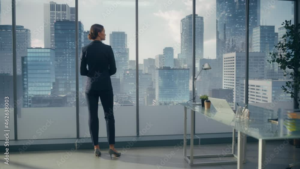 Successful Businesswoman in Stylish Suit Looking out of the Window at Big City in Downtown Area. Confident Female CEO Working on Investment Opportunity. Real Estate Agent Planning a Development Deal. Successful Businesswoman in Stylish Suit Looking out of the Window at Big City in Downtown Area. Confident Female CEO Working on Investment Opportunity. Real Estate Agent Planning a Development Deal.