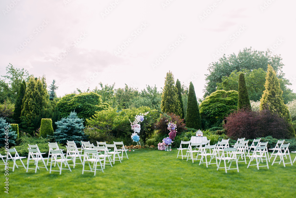 Wedding ceremony in the beautiful garden with wedding arch and white chairs.