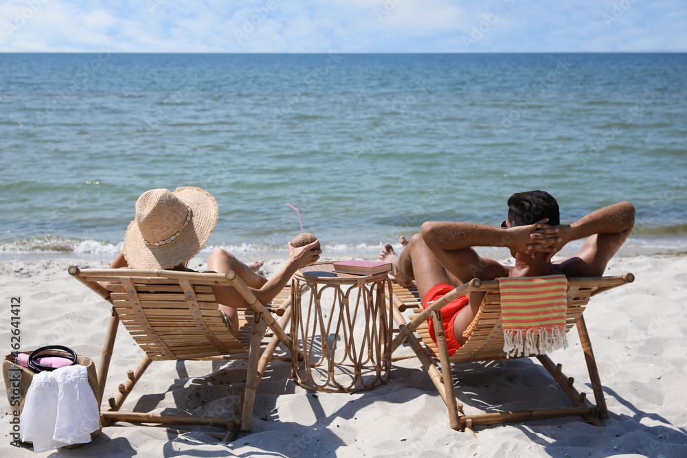 Couple resting in wooden sunbeds on tropical beach