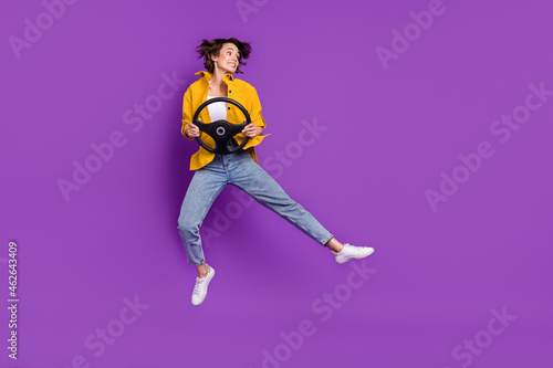 Photo of impressed funny young woman dressed yellow shirt smiling jumping high holding steering wheel isolated purple color background