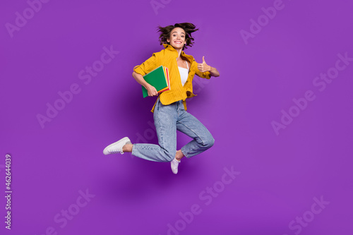 Photo of charming cute lady wear yellow shirt jumping high holding books showing thumb up isolated violet color background