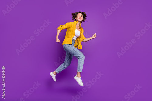 Photo of adorable shiny young woman dressed yellow shirt smiling jumping high running fast isolated purple color background