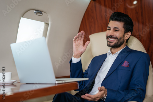 Quadro su tela Handsome smiling Arabian businessman using laptop computer having video call flying luxury private jet
