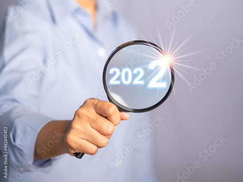 Hand of holding a magnifying glass looking to ideas for the 2022 year. Close-up photo. Selective focus. Space for text.