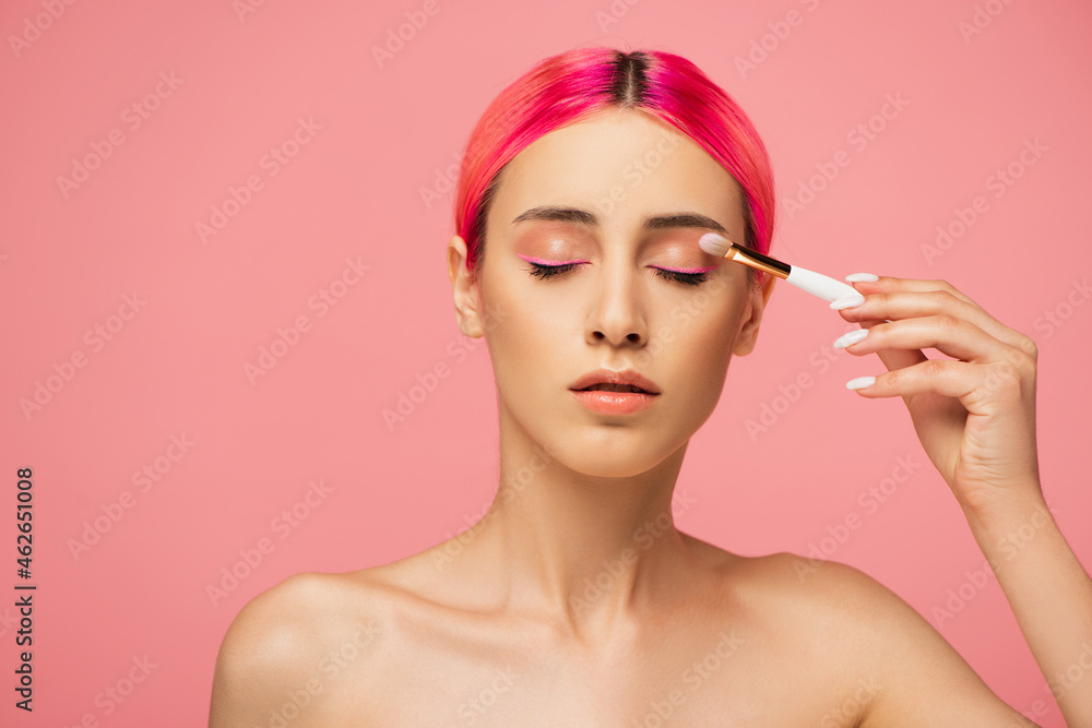 young woman with closed eyes applying eye shadow isolated on pink