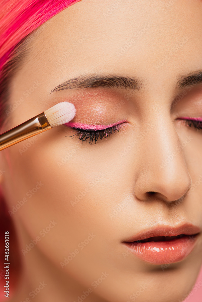 close up of young woman with closed eyes applying eye shadow