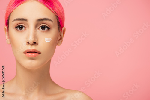 young woman with dyed hair and face cream on cheek isolated on pink