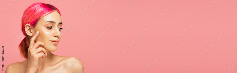 young woman with colorful hair applying face cream isolated on pink, banner