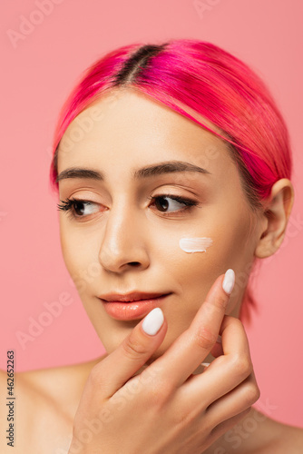 young woman with dyed hair applying face cream isolated on pink