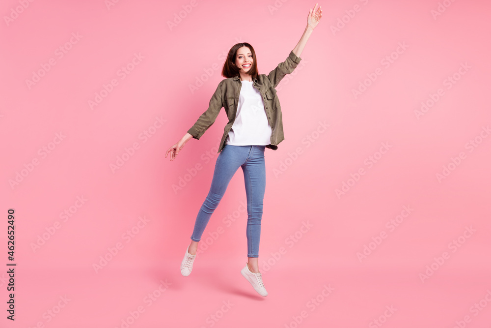 Full size photo of sweet short hairdo lady jump wear khaki shirt jeans sneakers isolated on pink color background Full size photo of sweet short hairdo lady jump wear khaki shirt jeans sneakers isolated on pink color background