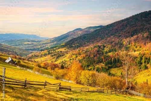 Village under the hills sheltered by autumn forests in the light of the bright sun in good weather