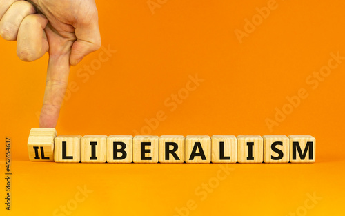 Illiberalism or liberalism symbol. Businessman turns a cube and changes the word 'illiberalism' to 'liberalism'. Beautiful orange background. Business, illiberalism or liberalism concept. Copy space. photo