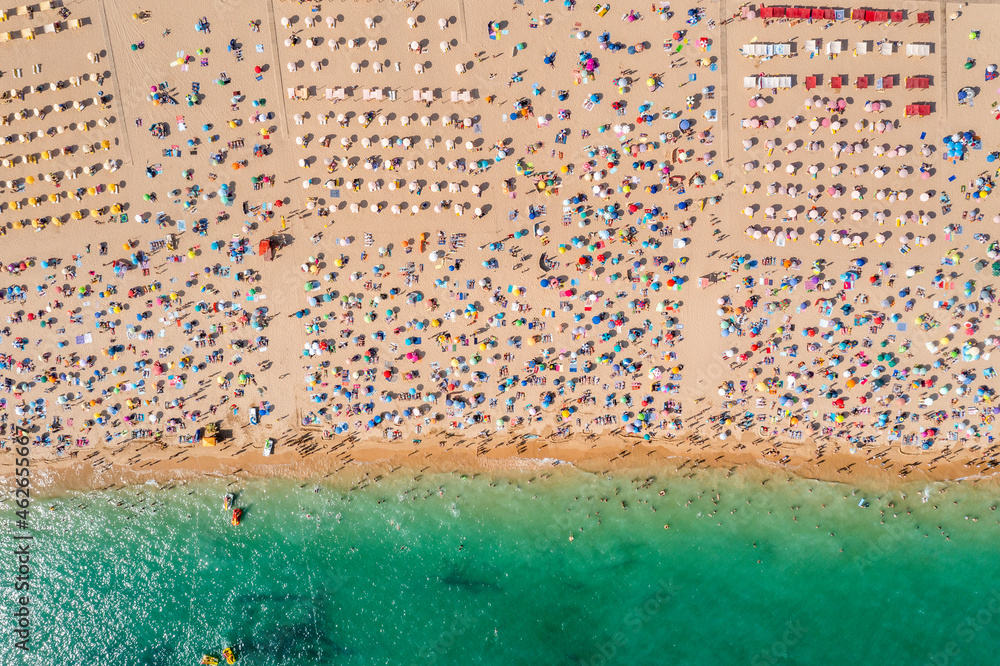 Drone shot of many people enjoying the beach and the ocean in high season- vacation pattern.
