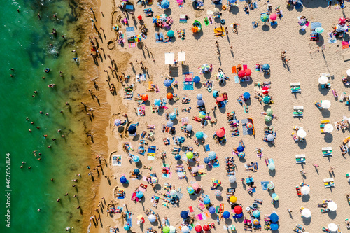 Drone shot of many people enjoying the beach and the ocean in high season- vacation pattern.