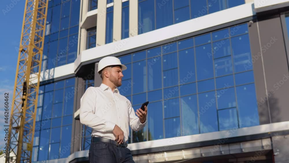 Engineer architect in a white shirt and helmet on the background of a modern glass building speaks on a cell phone. Modern construction Engineer architect in a white shirt and helmet on the background of a modern glass building speaks on a cell phone. Modern construction