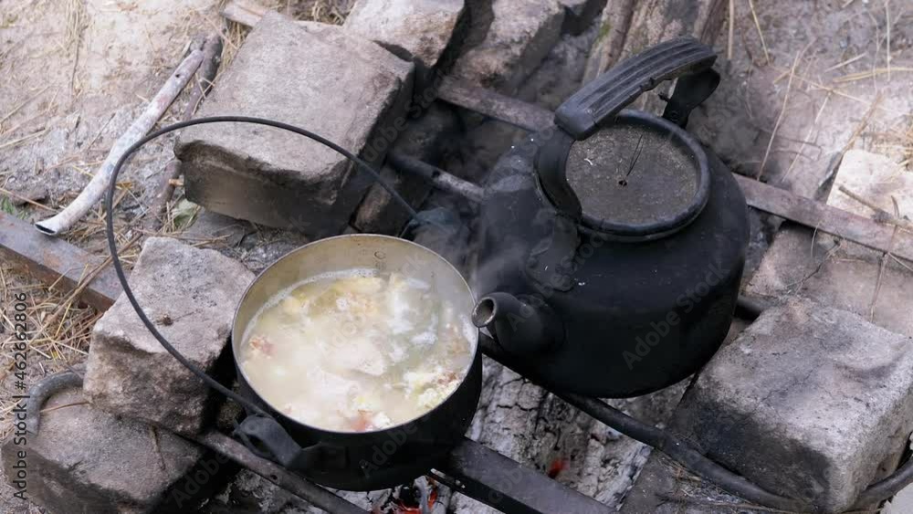 Preparing Food in a Saucepan on a Bonfire in Woods Outdoors. Boiling broth, water, soup is prepared on an open fire with a kettle. Concept of nutrition, survival, hiking, trip, travel in nature. Zoom. Preparing Food in a Saucepan on a Bonfire in Woods Outdoors. Boiling broth, water, soup is prepared on an open fire with a kettle. Concept of nutrition, survival, hiking, trip, travel in nature. Zoom.