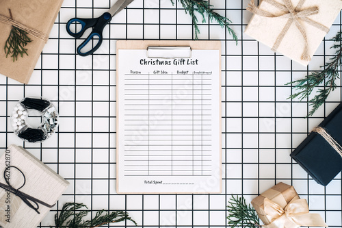 Modern flat lay with Christmas gift list. Keeping track gifts Christmas season. Clipboard with Christmas gift list, wrapped boxes and wrapping tools on white checkered background