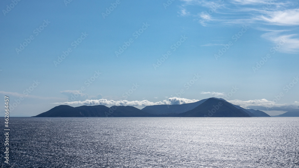 Blue Ionian sea landscape view on Lefkada Greece island. Bright day with low clouds over distant islands and contrast sunbeam on water