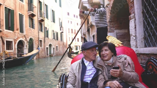 A beautiful mature married couple rides on a gondola boat in typical Venetian canals in Venice, in autumn, or winter. Italian gondolier.