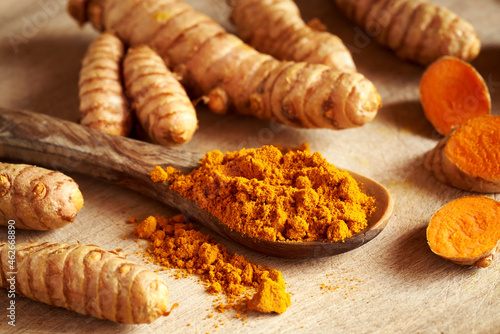 Ground turmeric powder on a spoon with fresh turmeric root