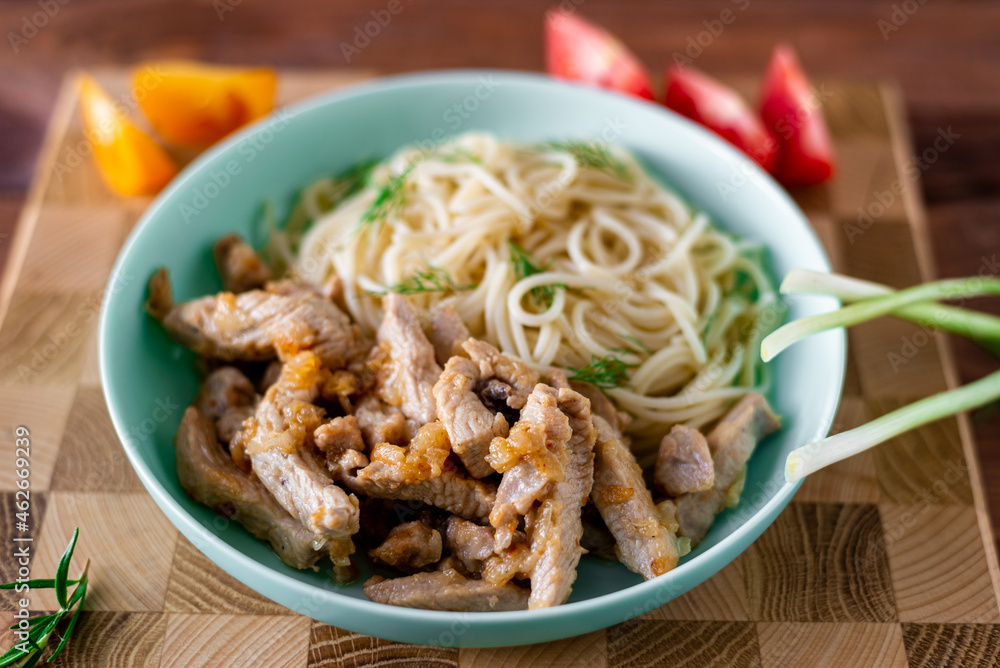 Fried meat and spaghetti on a plate on a wooden background with tomatoes and herbs.