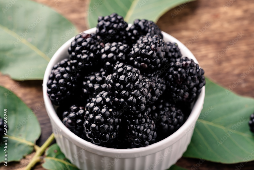 Fresh berries of blackberries in a white bowl on a wooden background close-up.