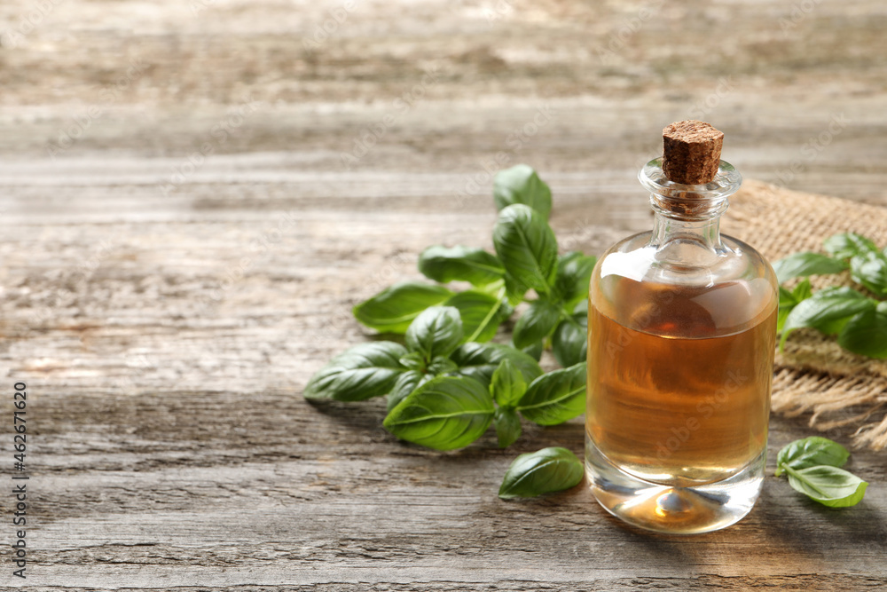 Glass bottle of basil essential oil and leaves on wooden table. Space for text Glass bottle of basil essential oil and leaves on wooden table. Space for text